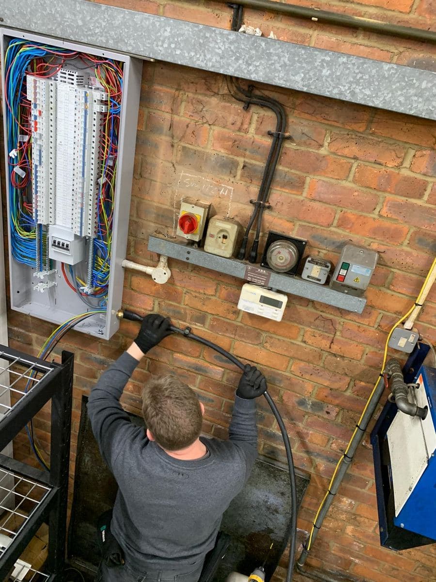 Electrician running armoured cable into a new three-phase distribution board on a brick wall