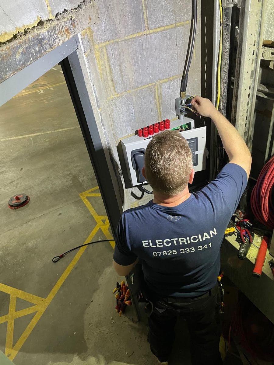 Electrician wiring a wall-mounted refuge and emergency telephone panel in a car park
