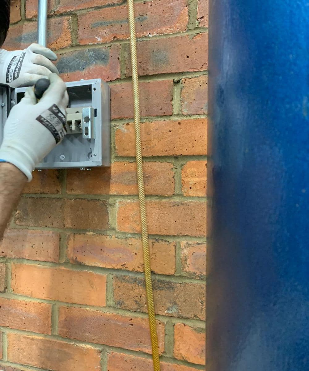 Gloved hands terminating cables in a metal-clad isolator on a brick wall